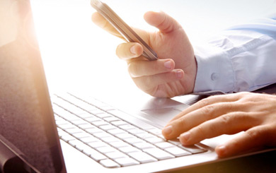 穿襯衫的男性在筆記型電腦前使用手機的手部特寫